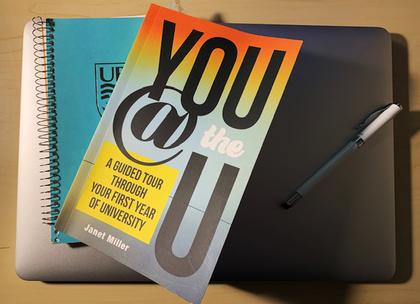 A photograph of the book You at the U with a teal blue notebook, both sitting on a silver laptop